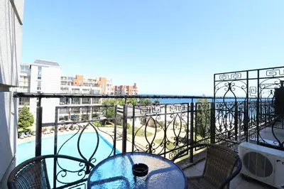 a balcony with a table and a view of a pool at Първа линия Апартаменти in Pomorie