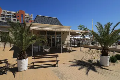 a building with two palm trees in front of it at Първа линия Апартаменти in Pomorie