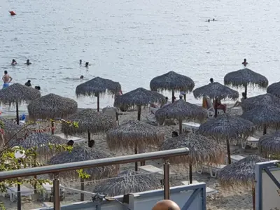 a beach with straw umbrellas and people in the water at Sveti Vlas Marina Beach Apartment - Vega Village in Sveti Vlas
