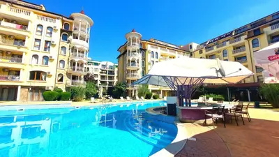 a swimming pool with a table and an umbrella and some buildings at Summer Dreams - Menada Apartments in Sunny Beach