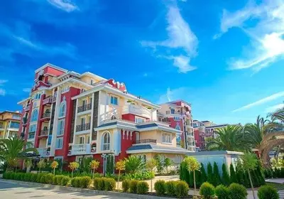 a large red and white building with palm trees at Messembria Resort in Sunny Beach