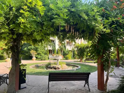 a park with a bench under a tree with a fountain at Deluxe Appartement in Cascadas Resort Sunny Beach in Sunny Beach