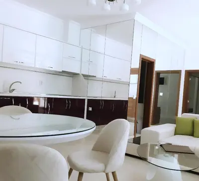a white kitchen with white chairs and a glass table at Апартамент в Комплекс Милениум in Pomorie