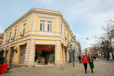 a man and woman walking down a street in front of a building at ПАЦО in Burgas City