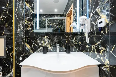 a bathroom with a white sink and black marble walls at M1 Pool and Beach View Apartment in Burgas City